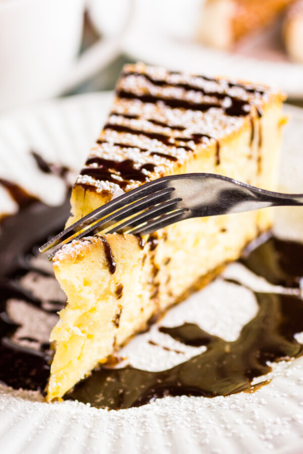 A slice of Bailey's Irish Cream Cheesecake on a plate and drizzled with chocolate ganache