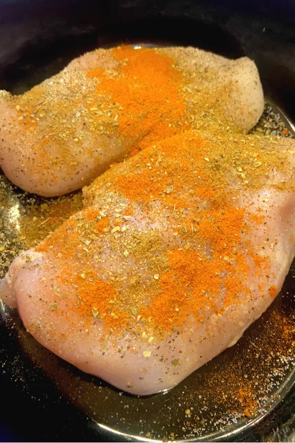 two chicken breasts in crock pot seasoned with spices