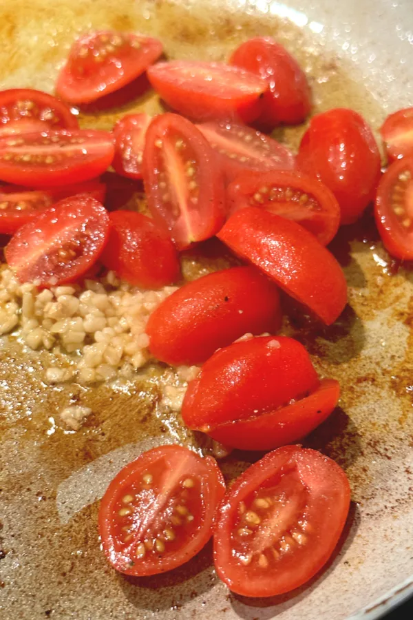 half grape tomatoes and garlic in skillet 