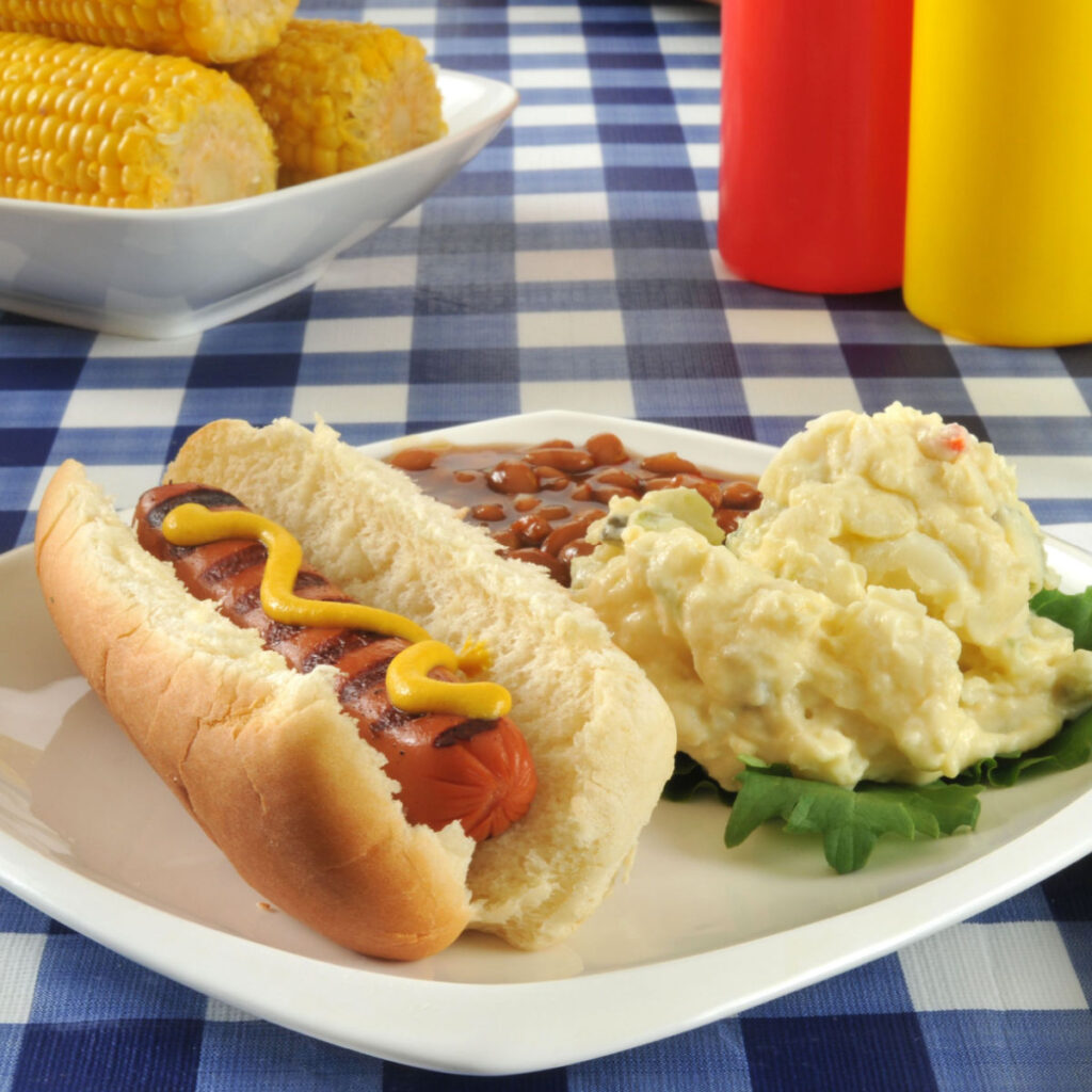 hot dog with potato salad and baked beans on white plate