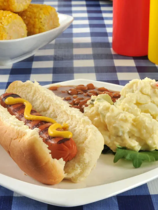 hot dog with potato salad and baked beans on white plate