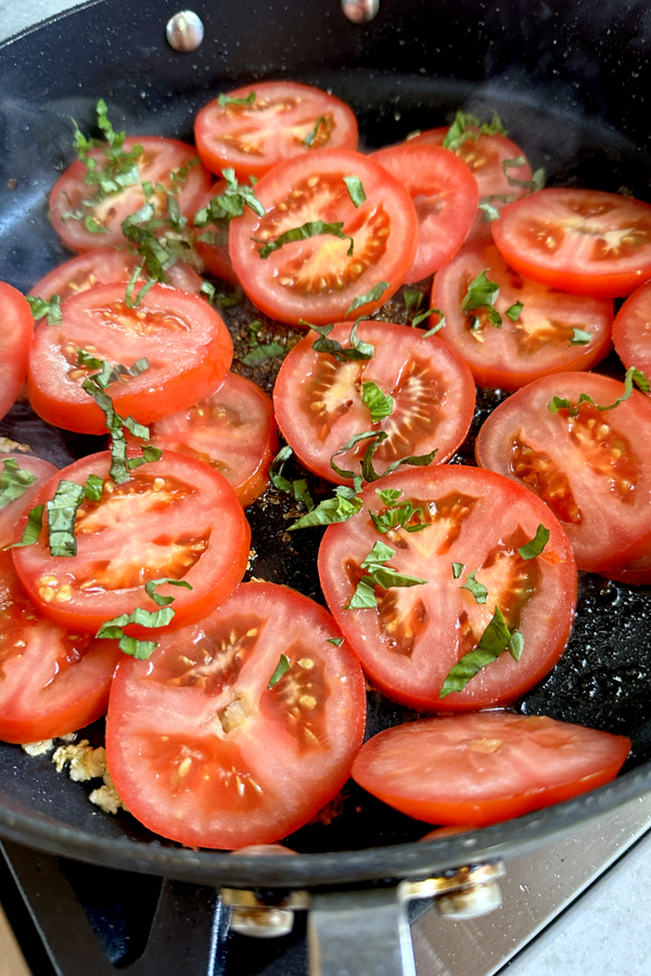 slices of tomato with slices of basil in a skillet 
