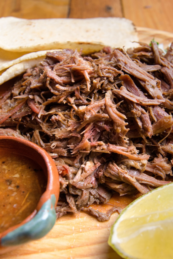 chuck roast made into shredded barbacoa meat on plate with lime and tortilla shells