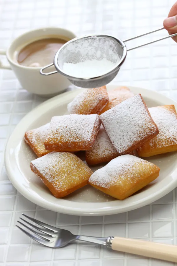 powder sugar in colander over donuts